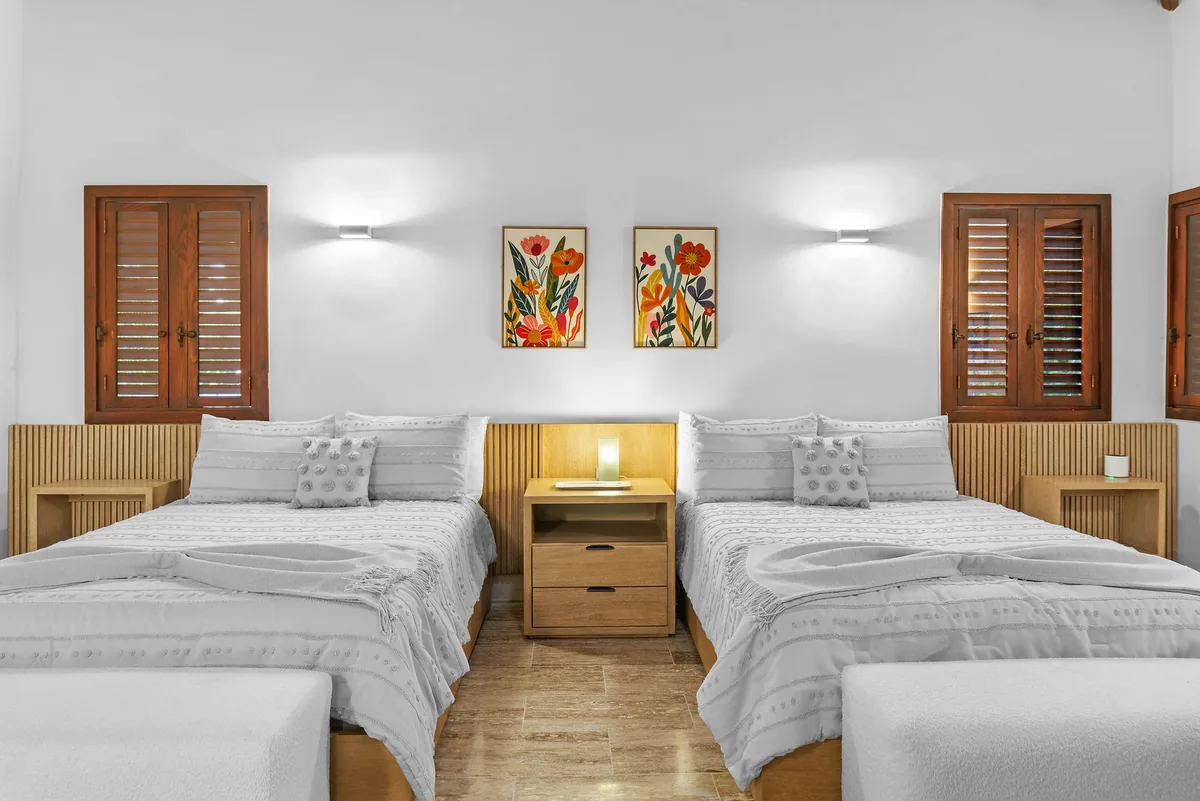 Guest bedroom with two queen beds, natural wood furniture and shuttered windows