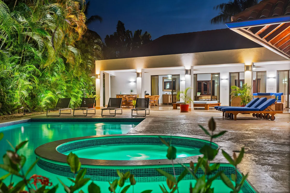 Illuminated pool and circular jacuzzi framed by tropical planting at dusk