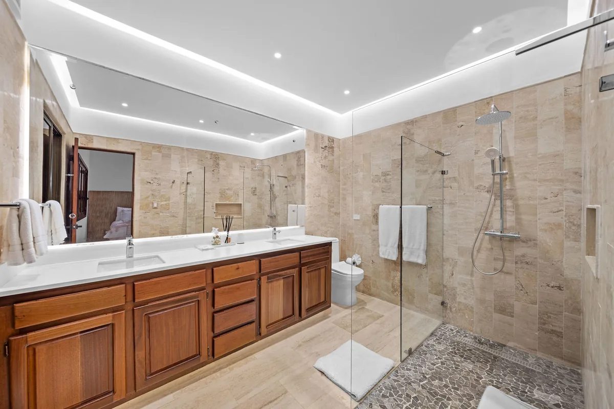 Stone-lined bathroom with double vanity, glass shower and rainfall fittings