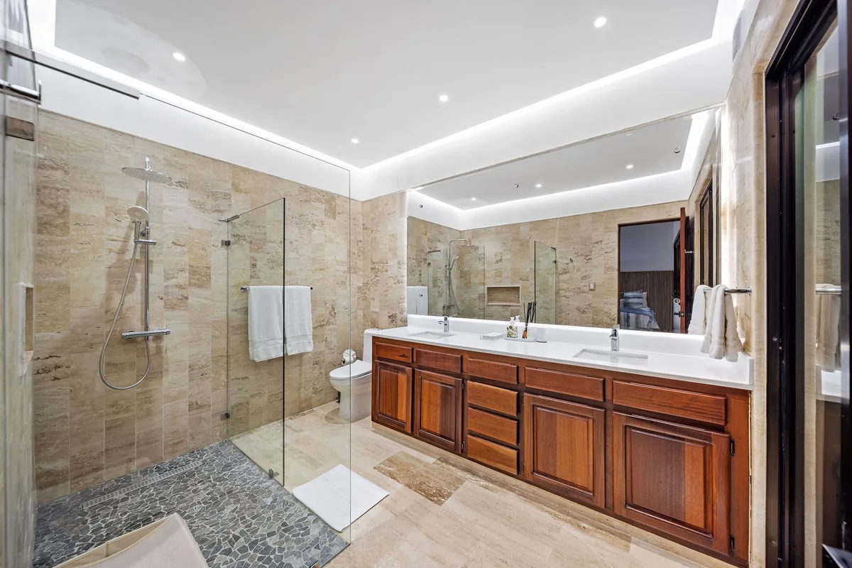 Stone bathroom with wood cabinetry, double vanity and glass shower